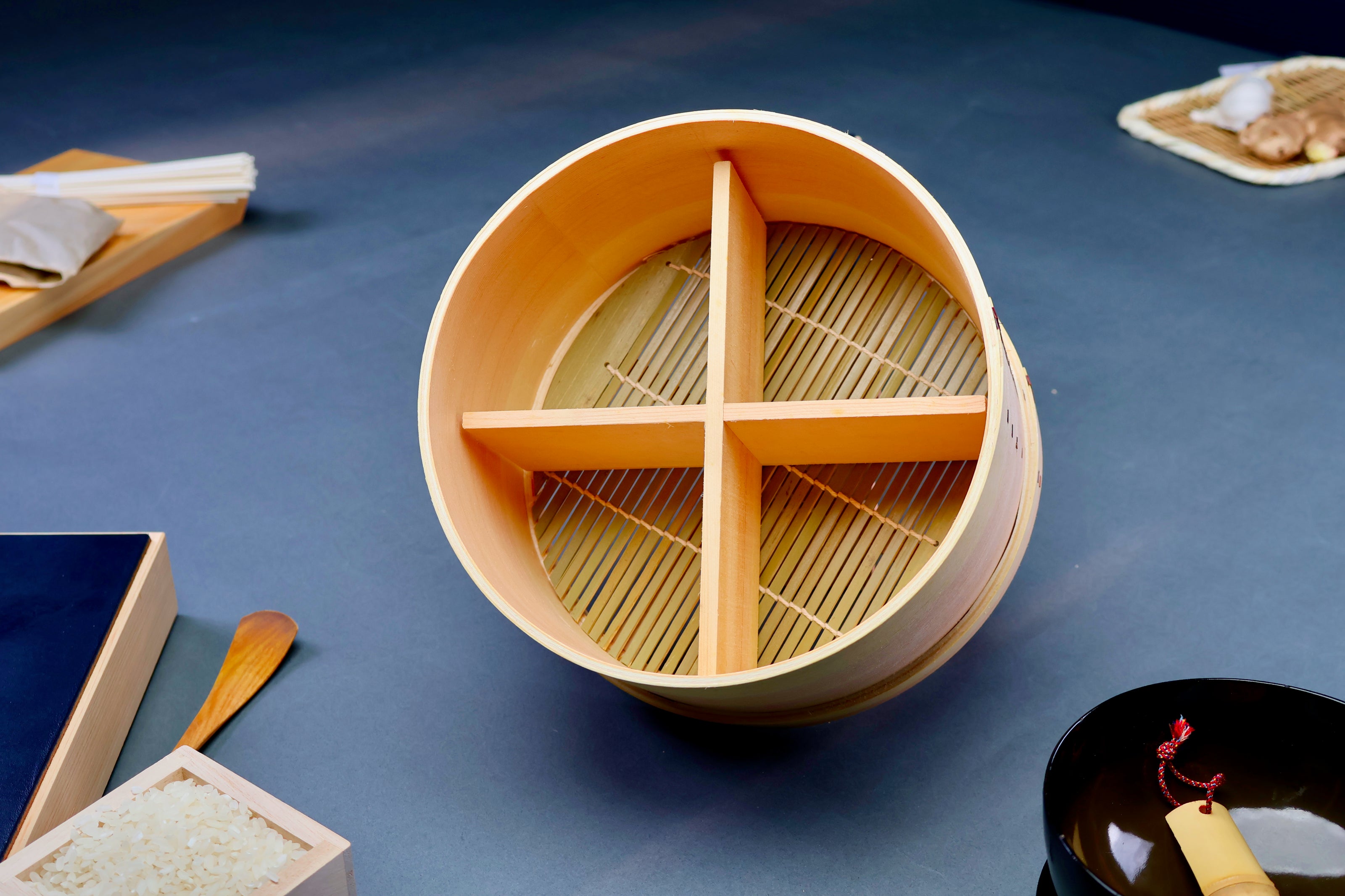 round natural wooden food steamer tilted showing interior wood divider bamboo mat around japanese kitchenware in grey background  
