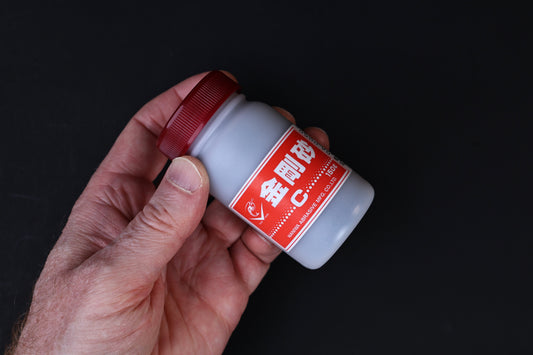 Naniwa abrasive powder 120 grit — held in hand at angle showing full red label and bottle construction