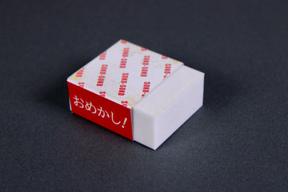 short rectangular white rust eraser partial wrapped product paper printed soko soko hiragana omekashi on dark grey background