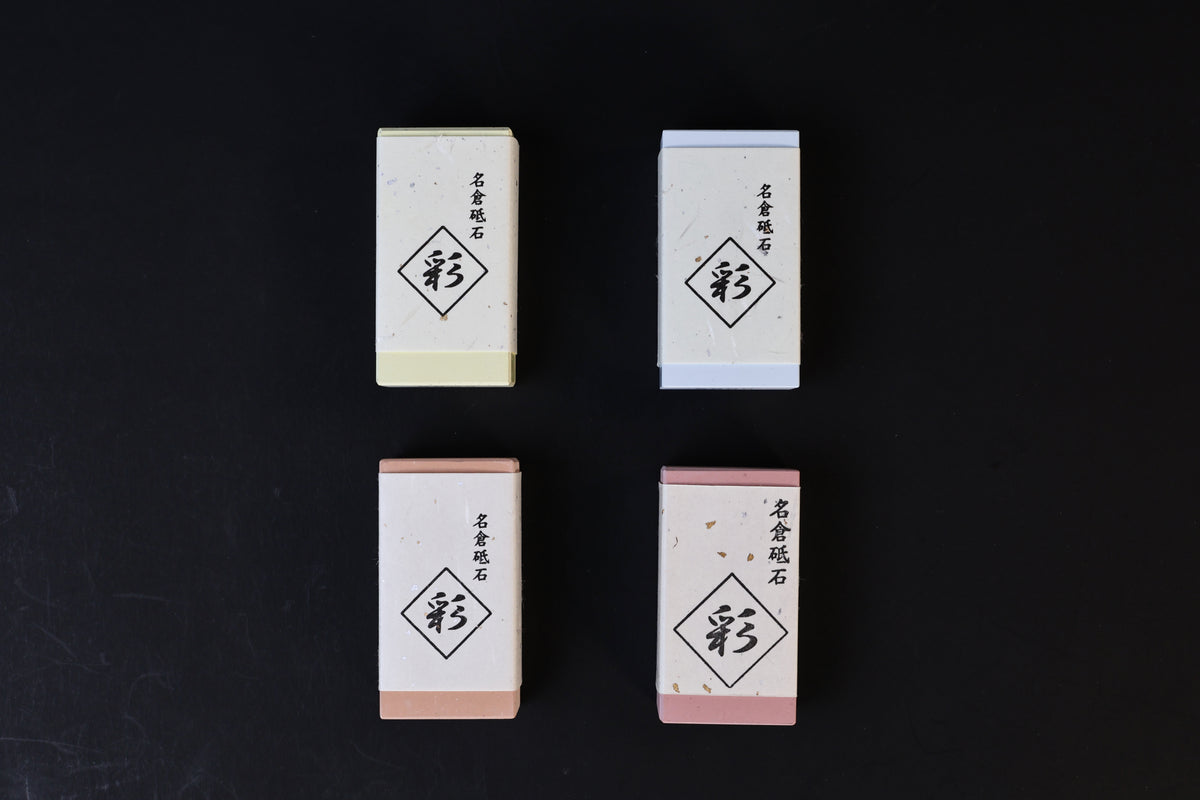 Four Naniwa Nagura stones in 2x2 overhead flat lay, showing yellow-green, blue, peach, and pink grit variations