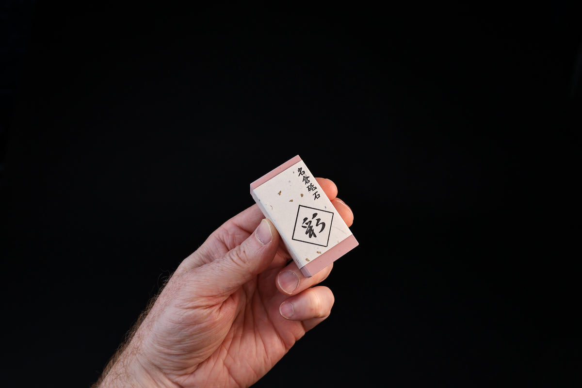 Naniwa Nagura stone with pink ends held in hand, showing compact rectangular form against black background