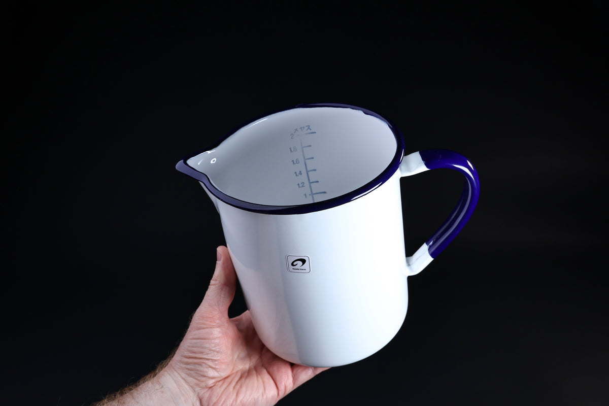 Noda Horo enamel measuring pitcher 2L — held at angle showing interior liter scale and cobalt blue rim