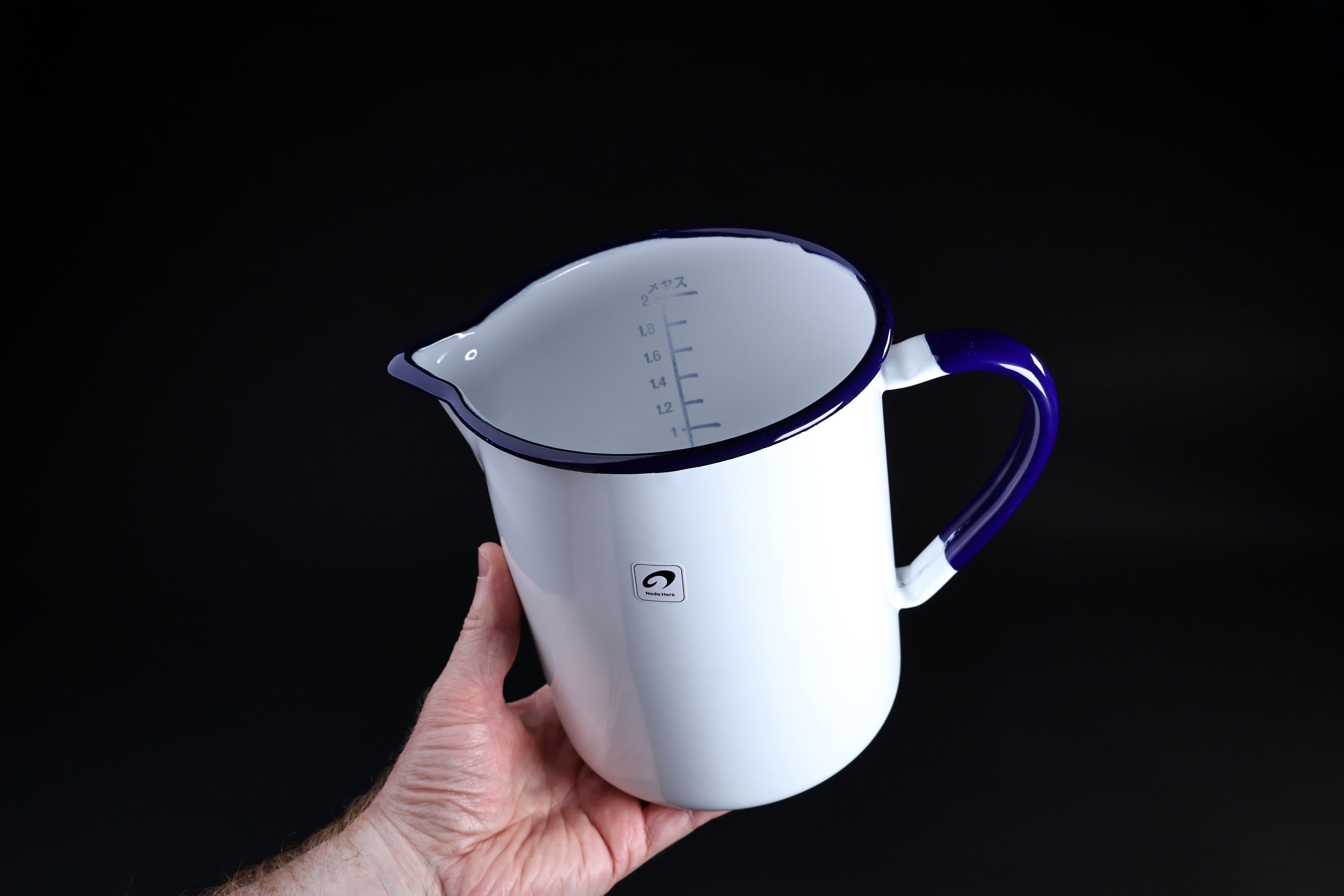 Noda Horo enamel measuring pitcher 2L — held at angle showing interior liter scale and cobalt blue rim