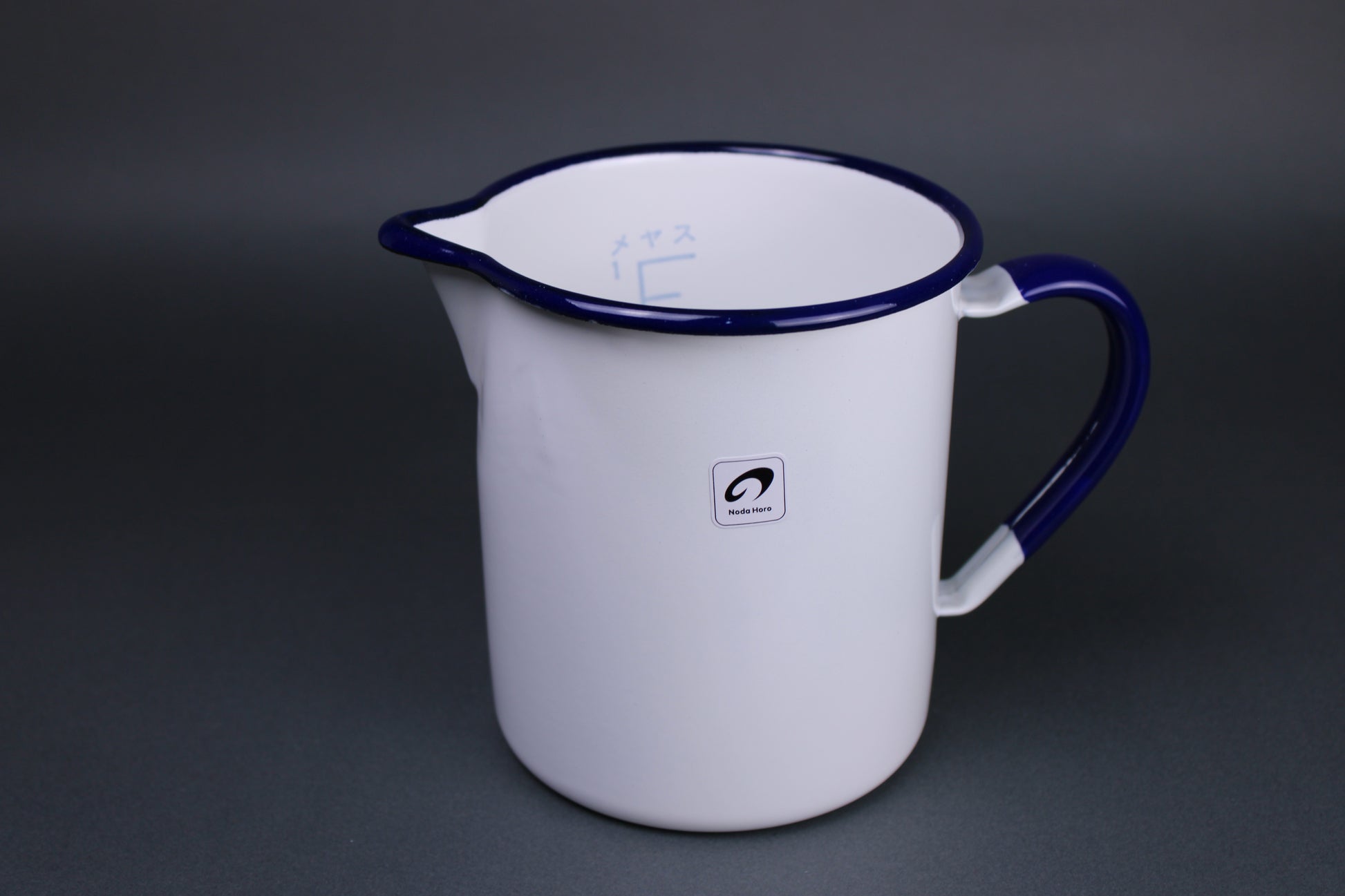frontal image of measuring cup handmade in japan with curved rim for pouring and handle glazed white and trimmed with blue navy glaze 