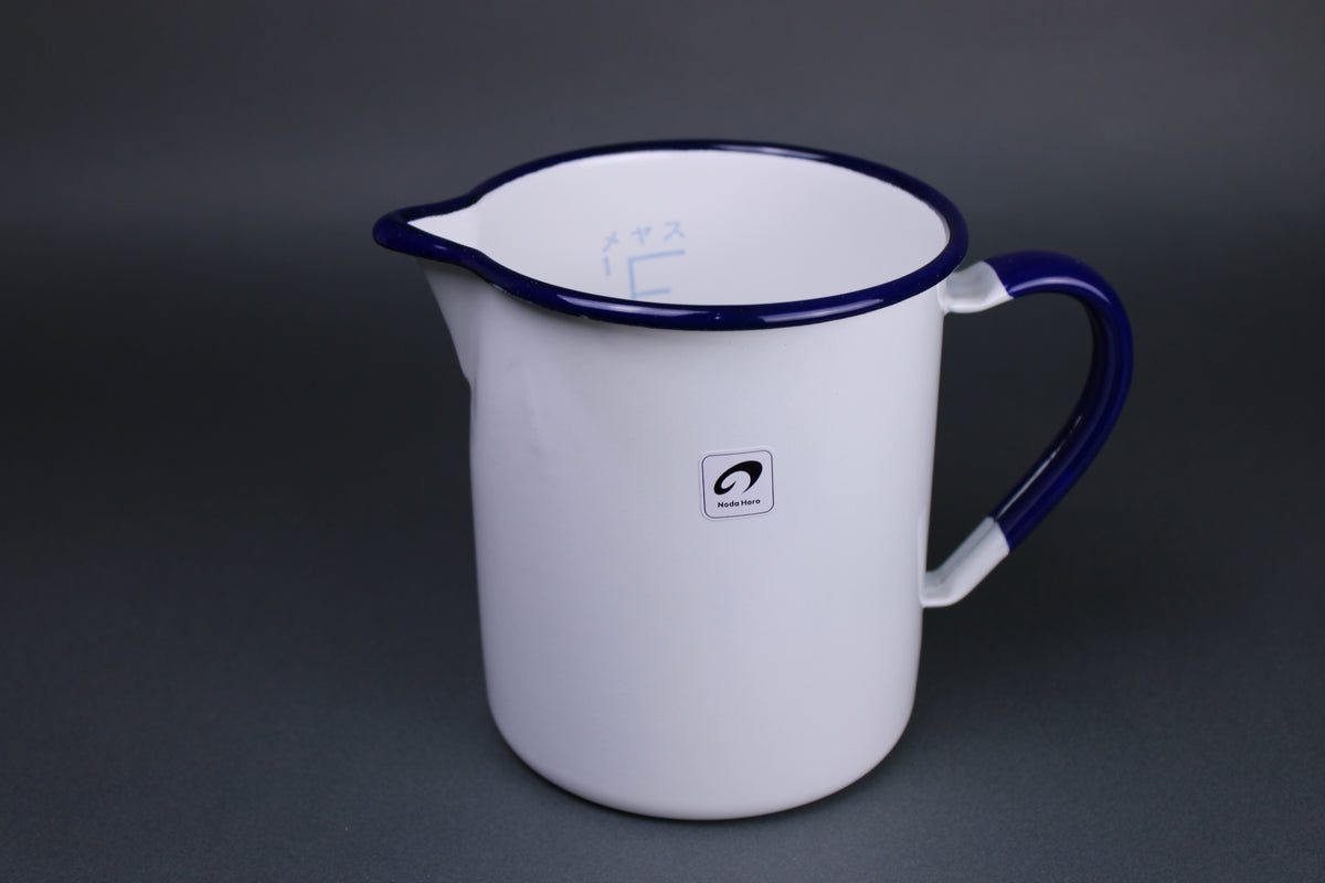 frontal image of measuring cup handmade in japan with curved rim for pouring and handle glazed white and trimmed with blue navy glaze 