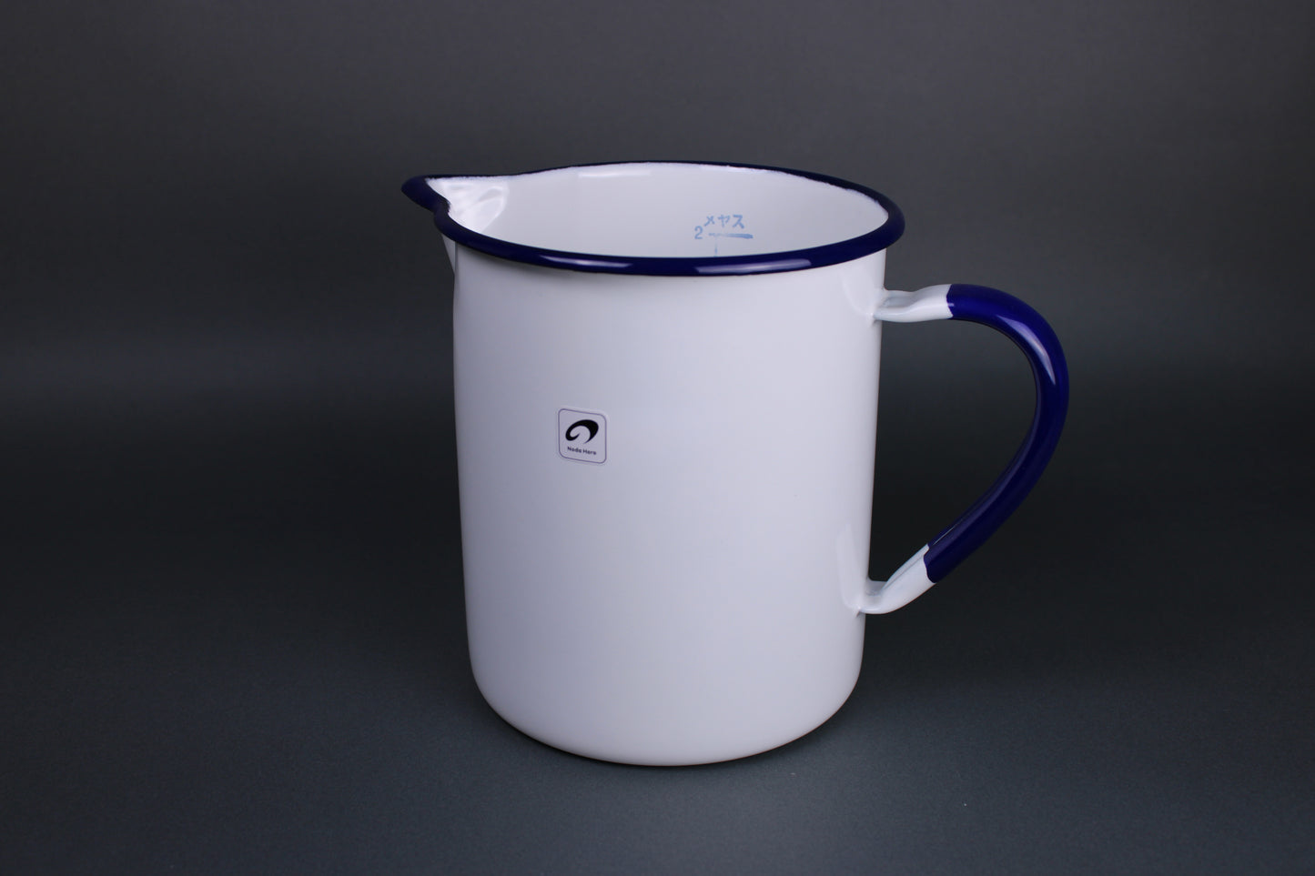 front facing view of two liter measuring cup with a curved rim for excellent pouring prominent white glazed surface with blue trim highlights on rim and handle measuring numbers and hiragana printed on inside of the cup there is a grey background 