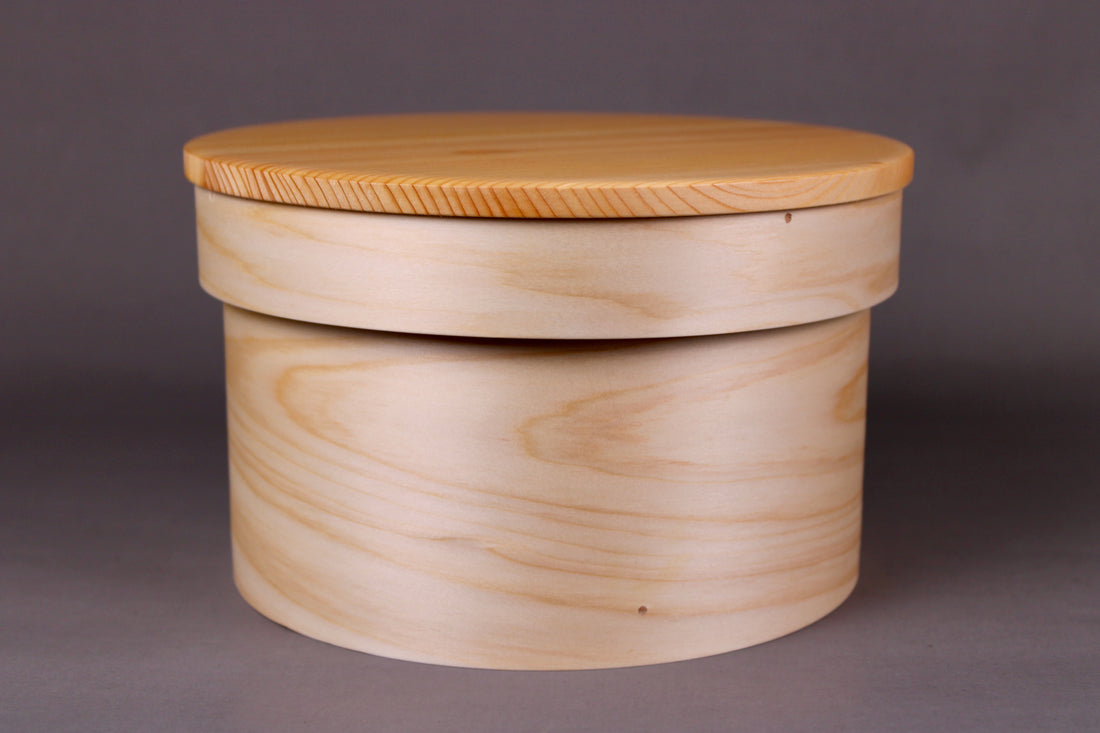 round hinoki wood container with natural wood tone lid on top in grey background