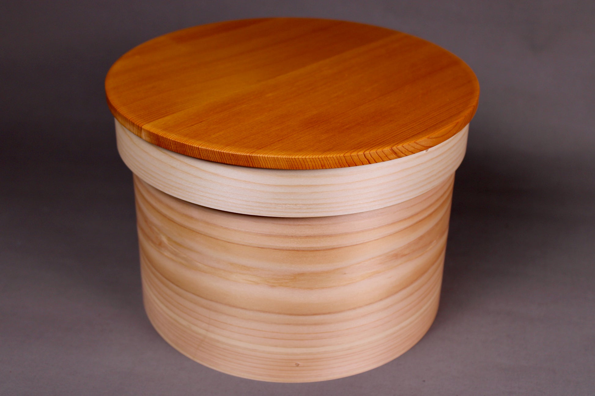 round hinoki wood container with natural wood tone lid on top in grey background