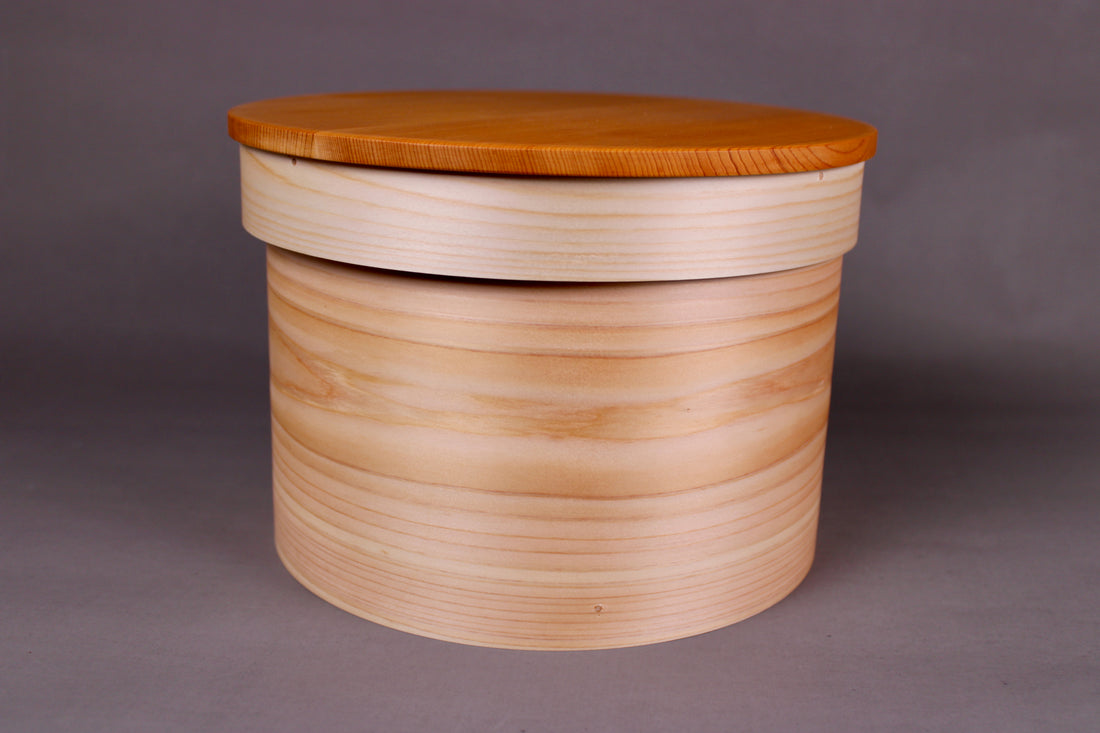 round hinoki wood container with natural wood tone lid on top in grey background