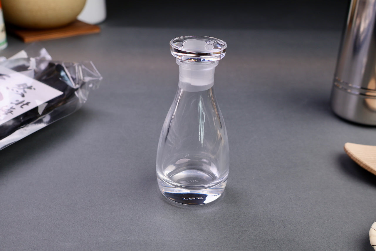 glass cruet clear shiny circular lid beside long body container with grey background