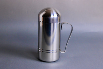 cylinder shaped stainless steel oil dispenser with curved handle in grey background 