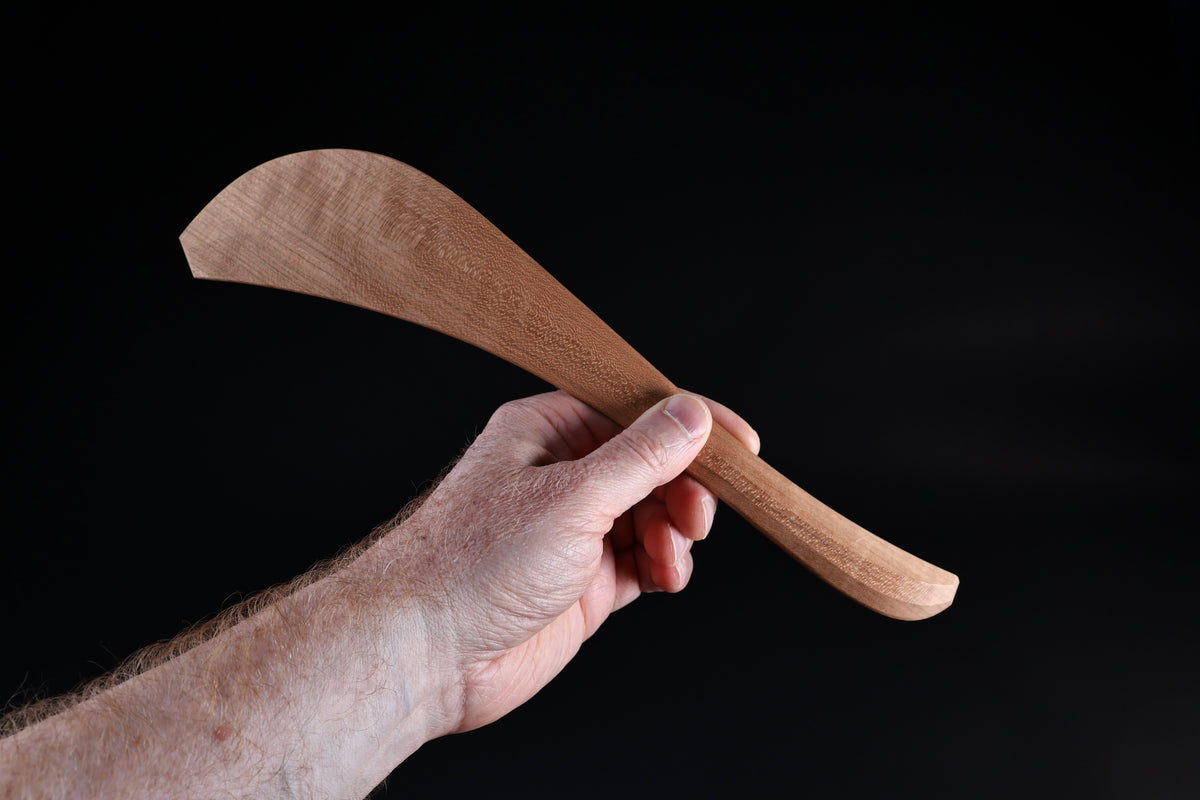 Okubo House cherry wood spatula held upright in hand, showing wide blade shape and curved handle from front