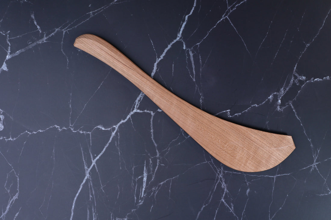 Okubo House handmade cherry wood spatula flat lay on marble, showing full curved profile and wood grain