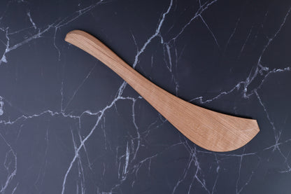Okubo House handmade cherry wood spatula flat lay on marble, showing full curved profile and wood grain