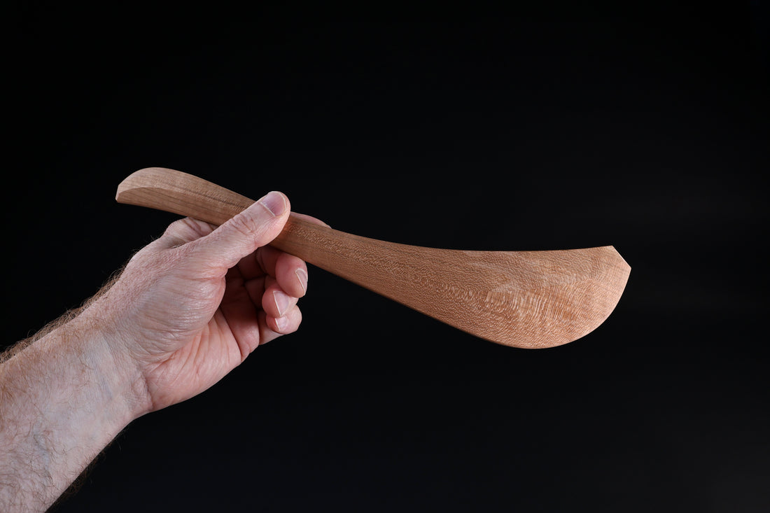 Okubo House cherry wood spatula held in hand, blade face showing wood grain texture and curved form