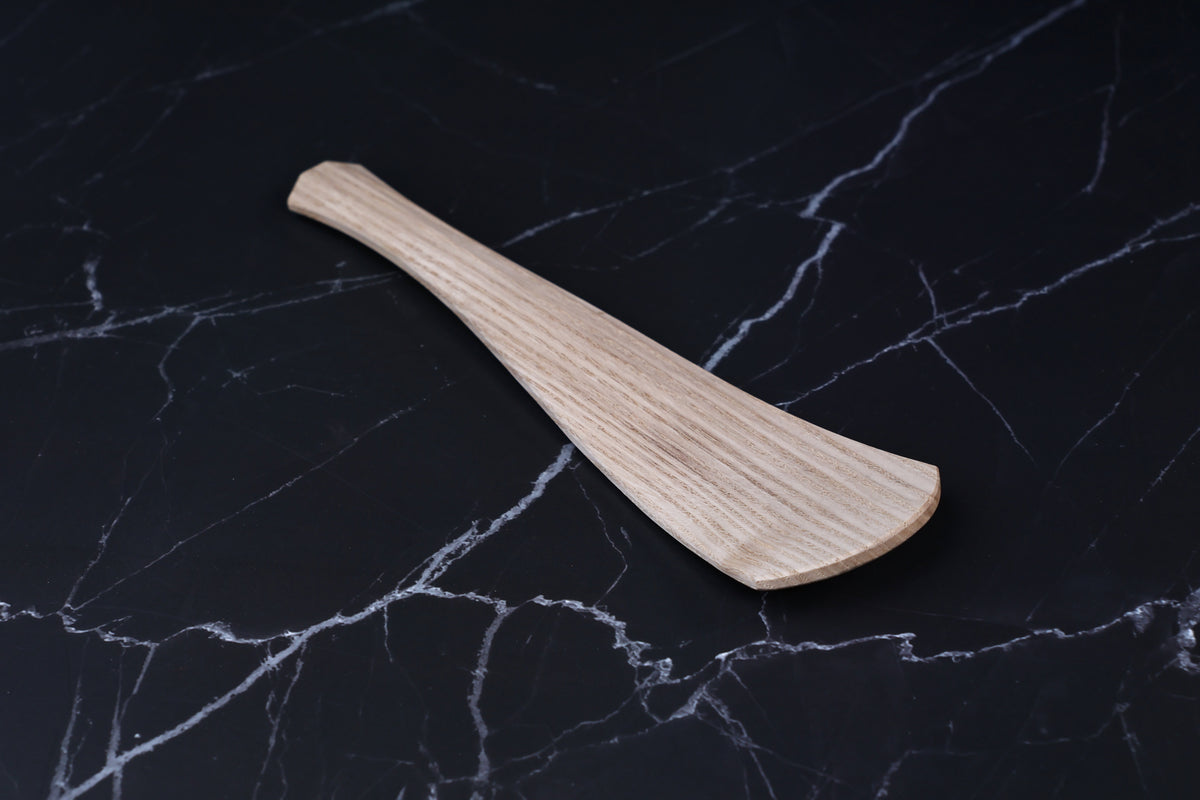 Okubo House chestnut rice paddle — angled view showing paddle face, handle taper, and chestnut grain on black marble