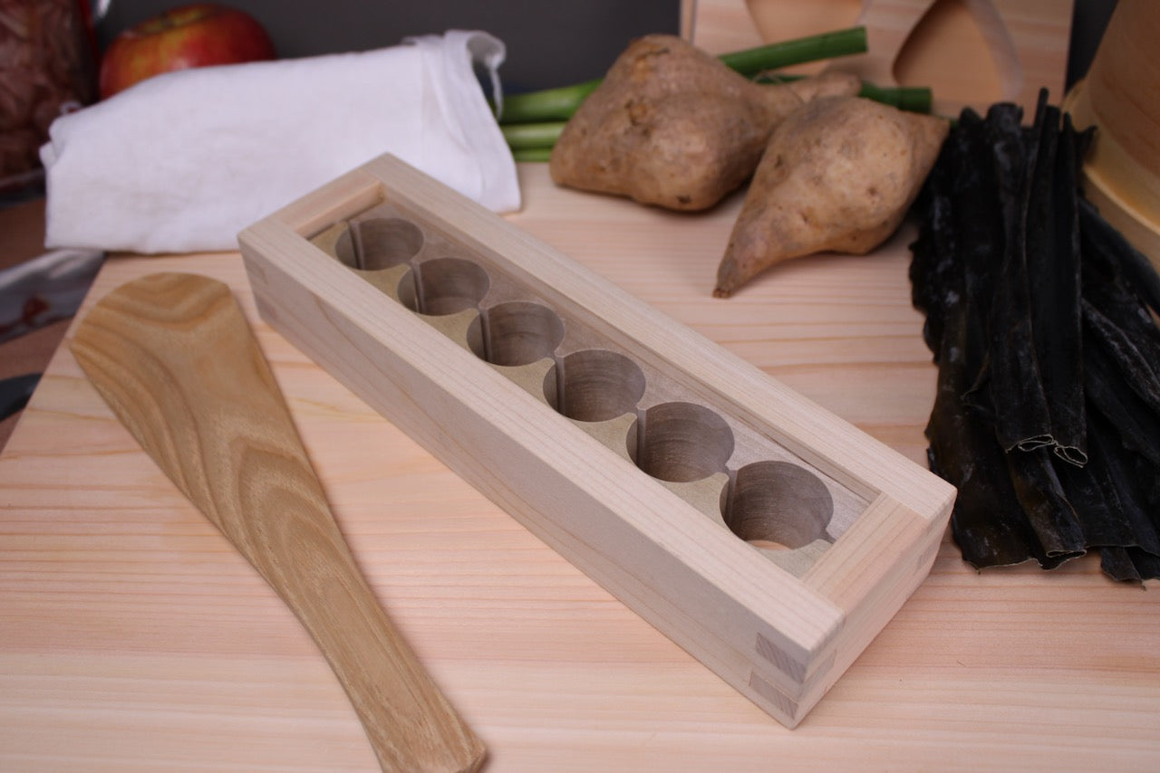 makunouchi onigiri mold on hinoki cutting board beside okubo house rice scoop kitchen background