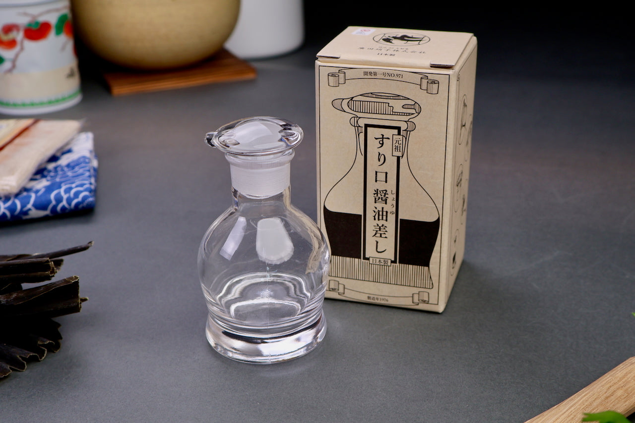 hirota glass original soy sauce cruet bulbous short body with circular lid next to tan white product box hiragana characters and animation with grey backdrop