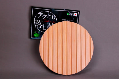 back side with ridges circular wood drop lid with long shallow handle yellowish gold hue beside black product tag with hiragana in front of grey background