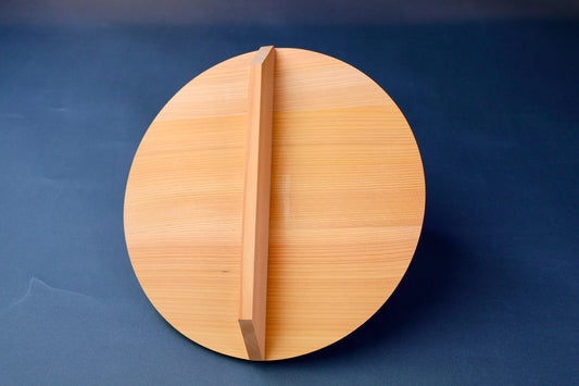 circular wood drop lid with long shallow handle yellowish gold hue in front of bluish background