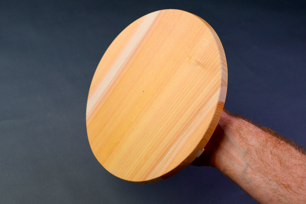 handle holding round wood lid showing underside of lid with wooden natural lines in grey background