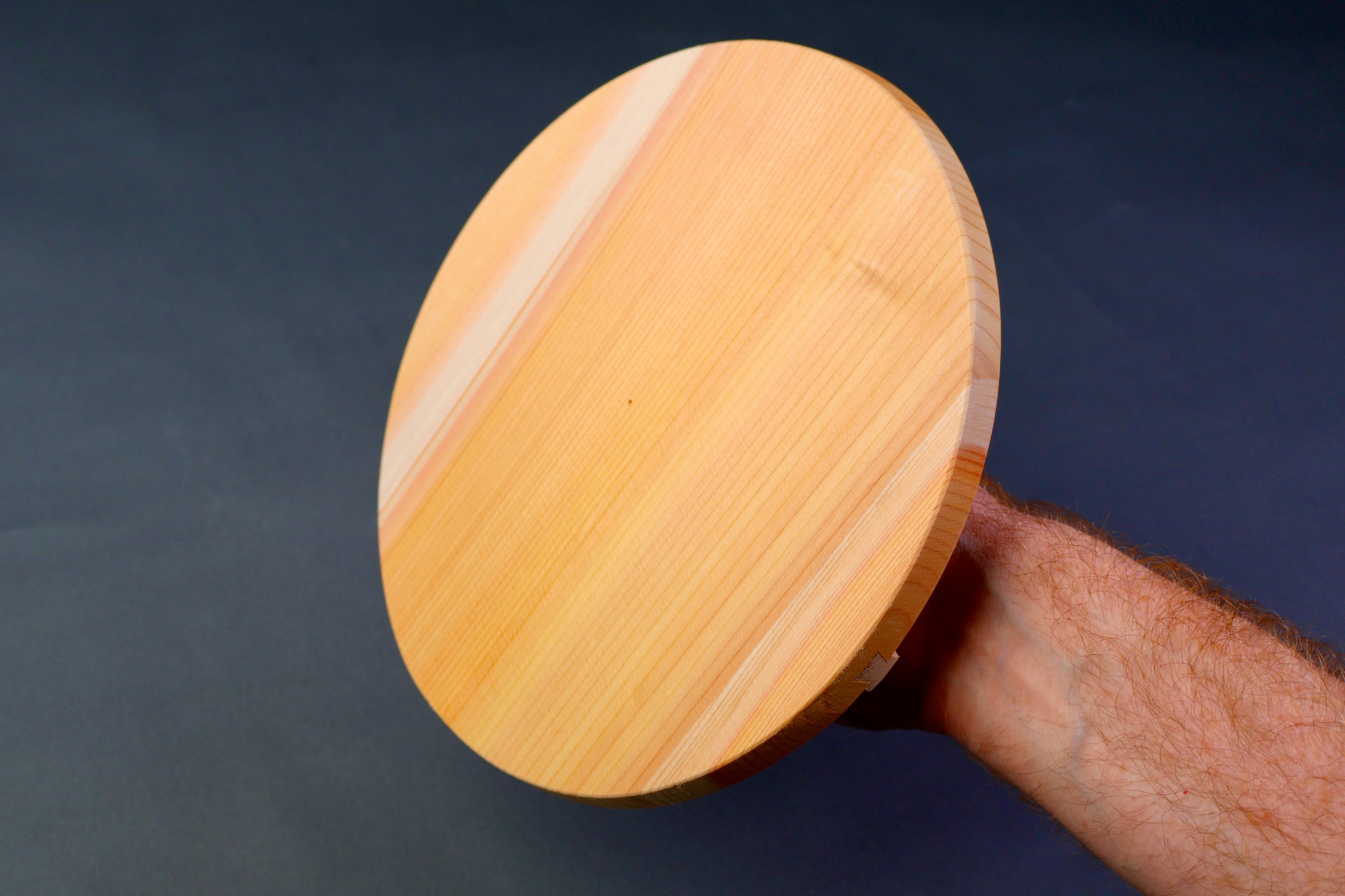handle holding round wood lid showing underside of lid with wooden natural lines in grey background
