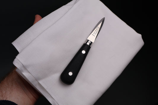 made in france small sized black handled beveled short bladed knife held in hand on top of white cloth black background