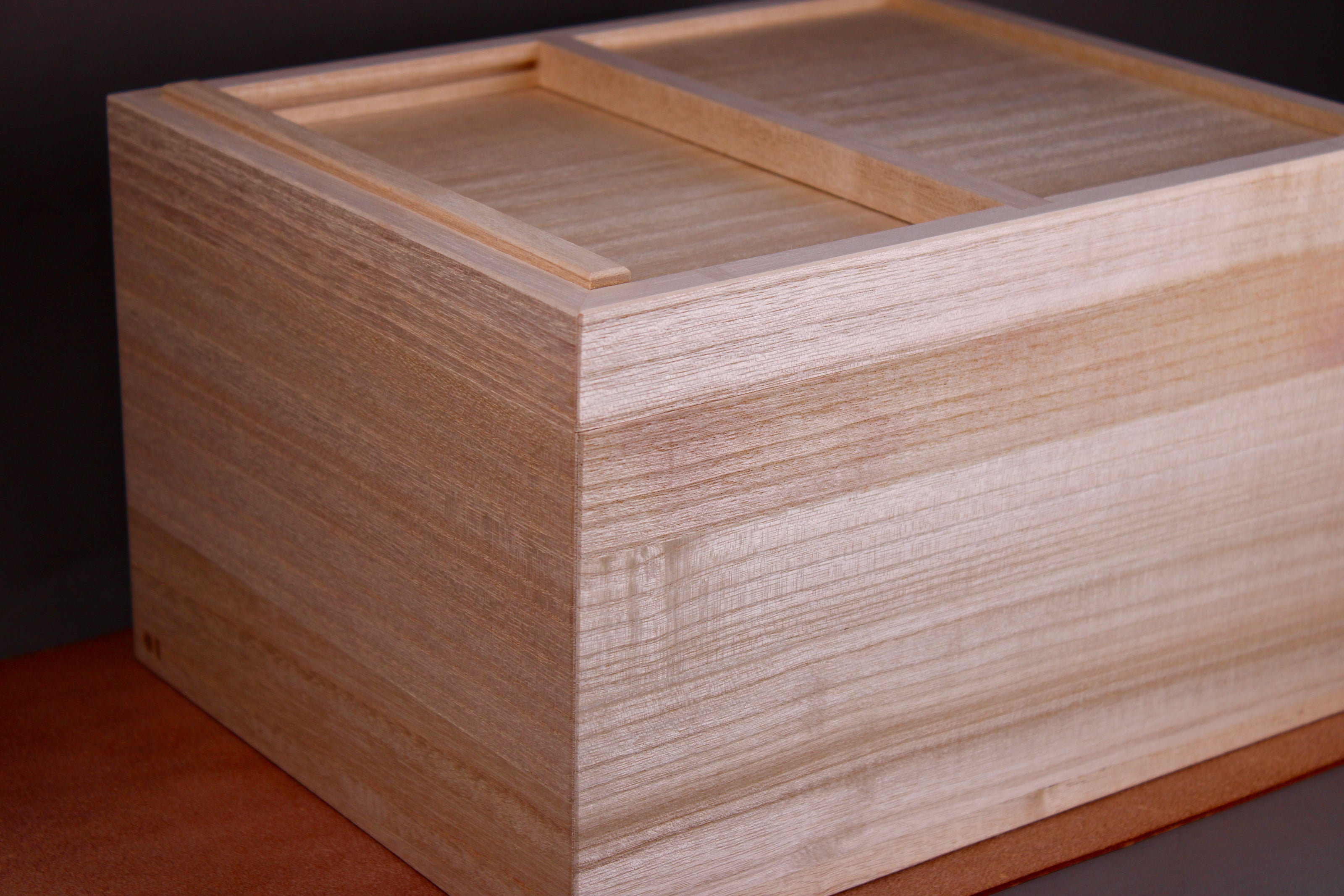 tall rectangular paulownia wood rice box sliding door on top sitting on dark brown leather surface dark grey background