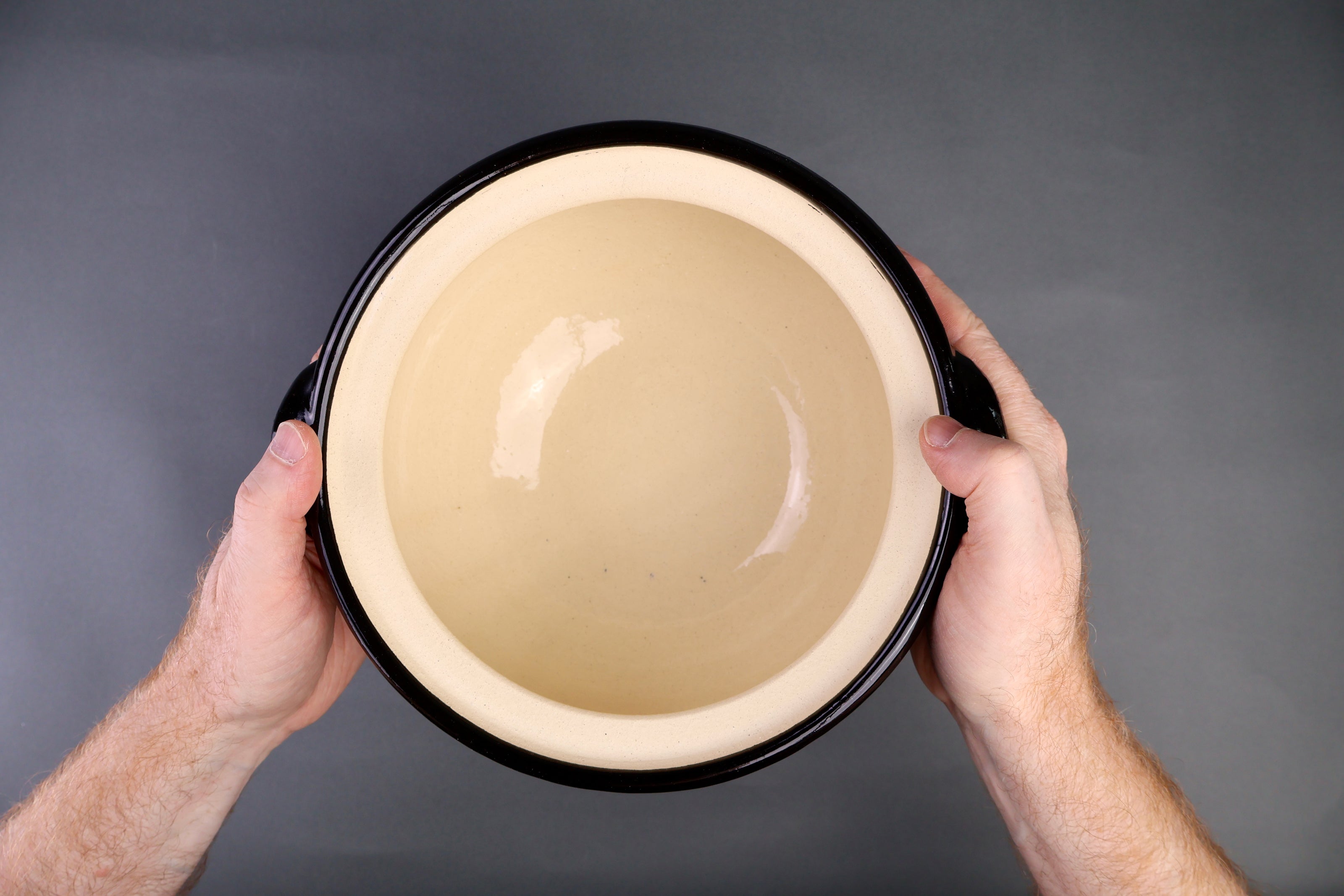 hand holding rice donabe container without lid surface is partially black glazed and unglazed grey background