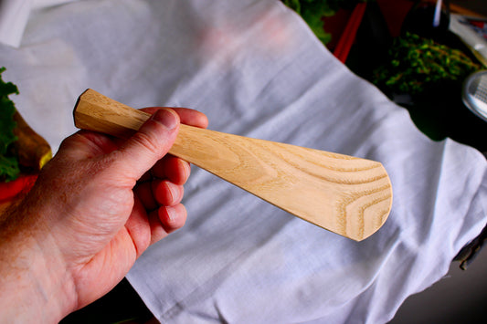 hand holding a long wooden tan rice scoop spoon showing wood grain on white cloth background with kitchenware 