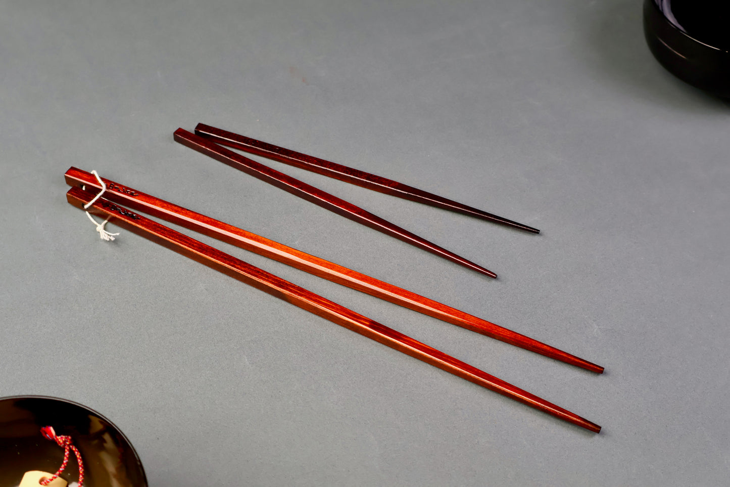 two pair of urushi dark brown chopsticks one long one short for cooking in light grey background