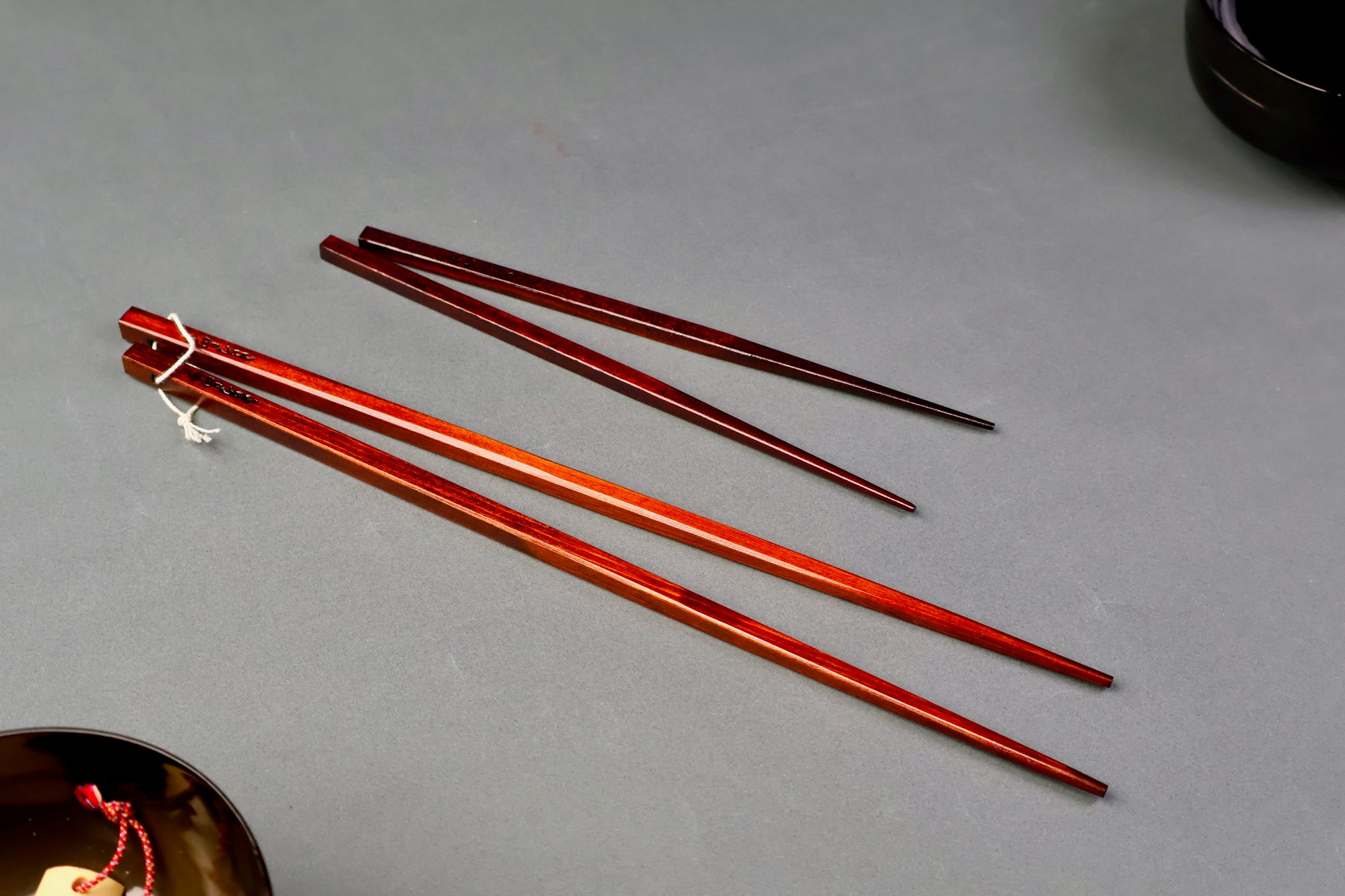 two pair of urushi dark brown chopsticks one long one short for cooking in light grey background
