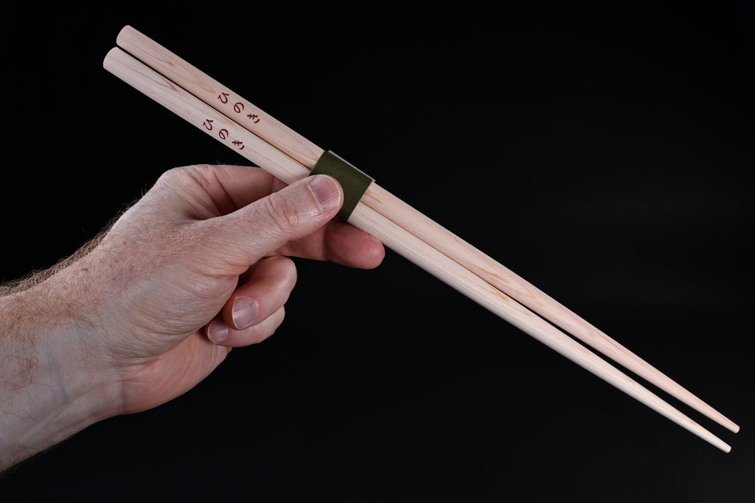 Saibashi round cooking chopsticks — held in hand showing grip position, kanji stamp and green band visible