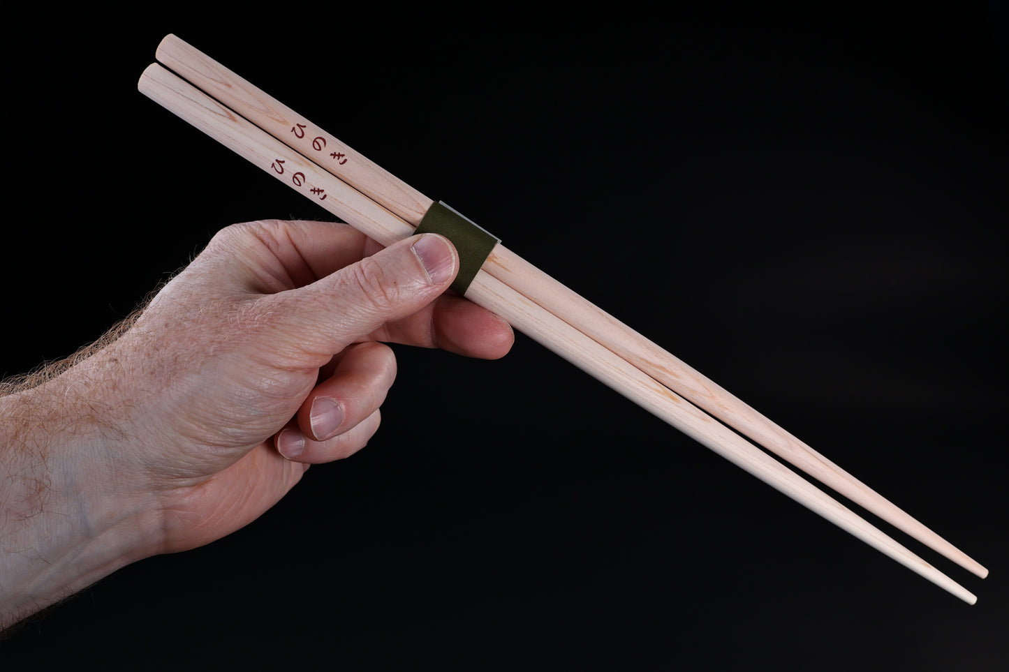 Saibashi round cooking chopsticks — held in hand showing grip position, kanji stamp and green band visible