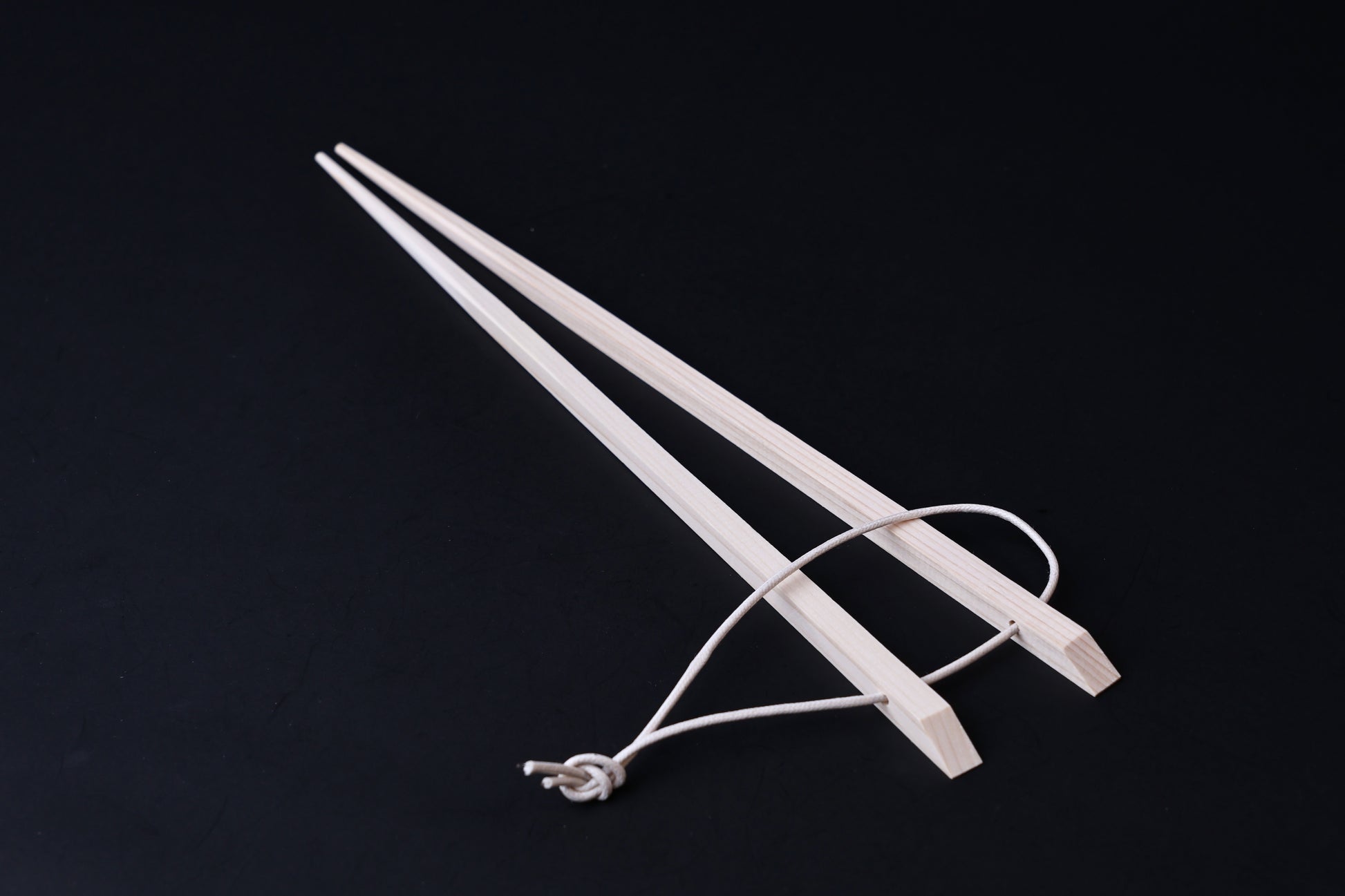 Saibashi square cooking chopsticks — full length angled view, handle end down showing square profile and hanging cord