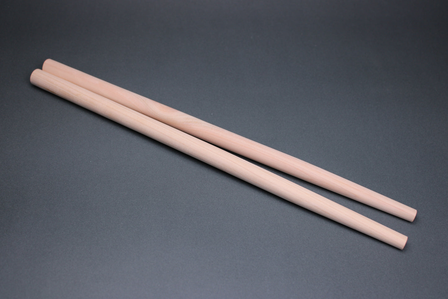 long thick round hinoki wood cooking chopsticks sit parallel on dark grey background