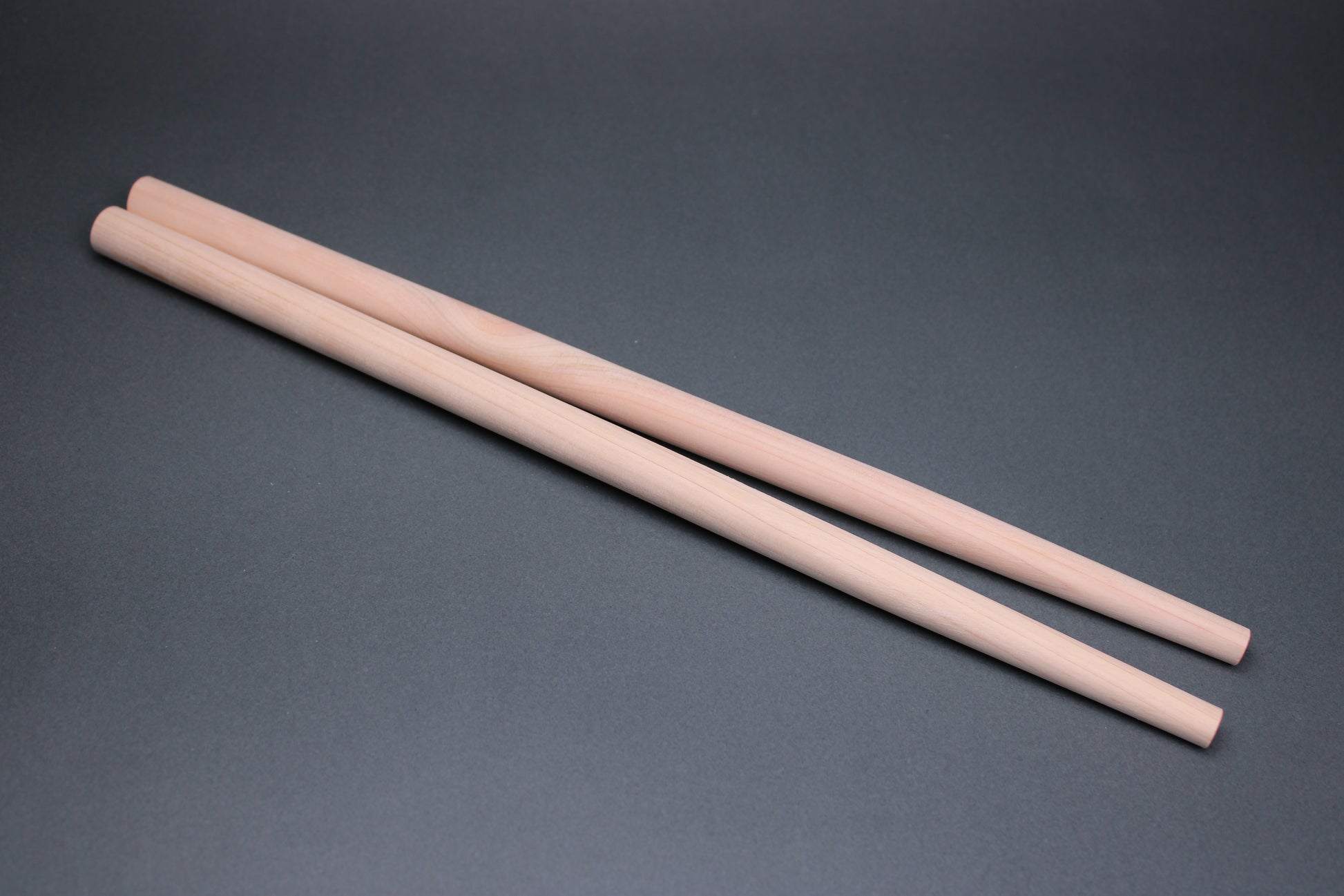 long thick round hinoki wood cooking chopsticks sit parallel on dark grey background