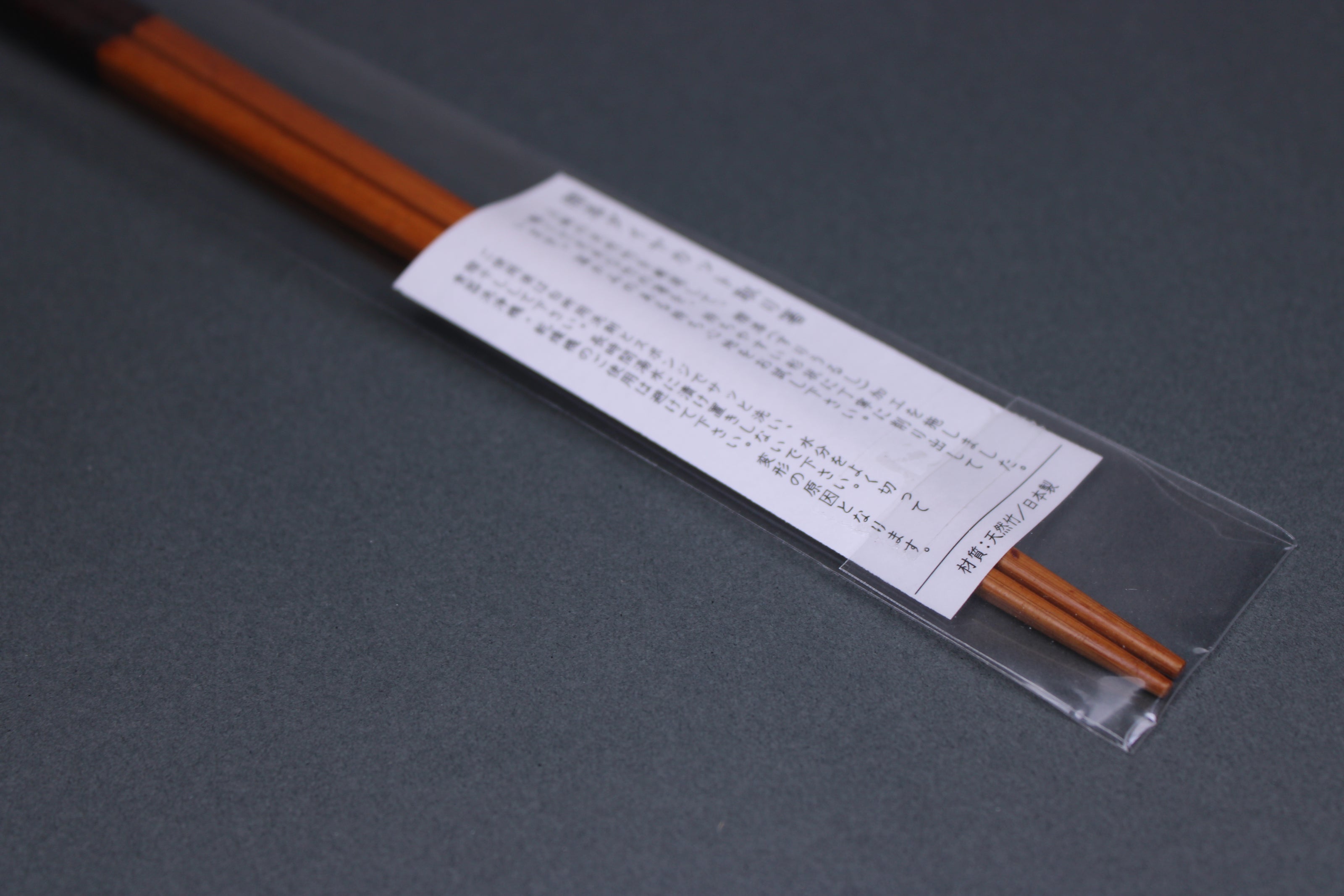 long square brownish tan bamboo cooking chopsticks urushi lacquered in clear packaging white product paper description in hiragana grey backdop