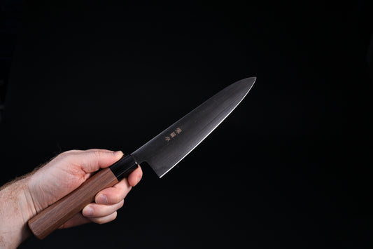 Sakai Kikumori Wasiki gyuto 210mm — held in hand, blade side showing kanji engraving and walnut wa handle
