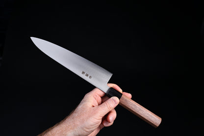Sakai Kikumori Wasiki gyuto 210mm — held in hand, spine side showing full blade profile and walnut handle