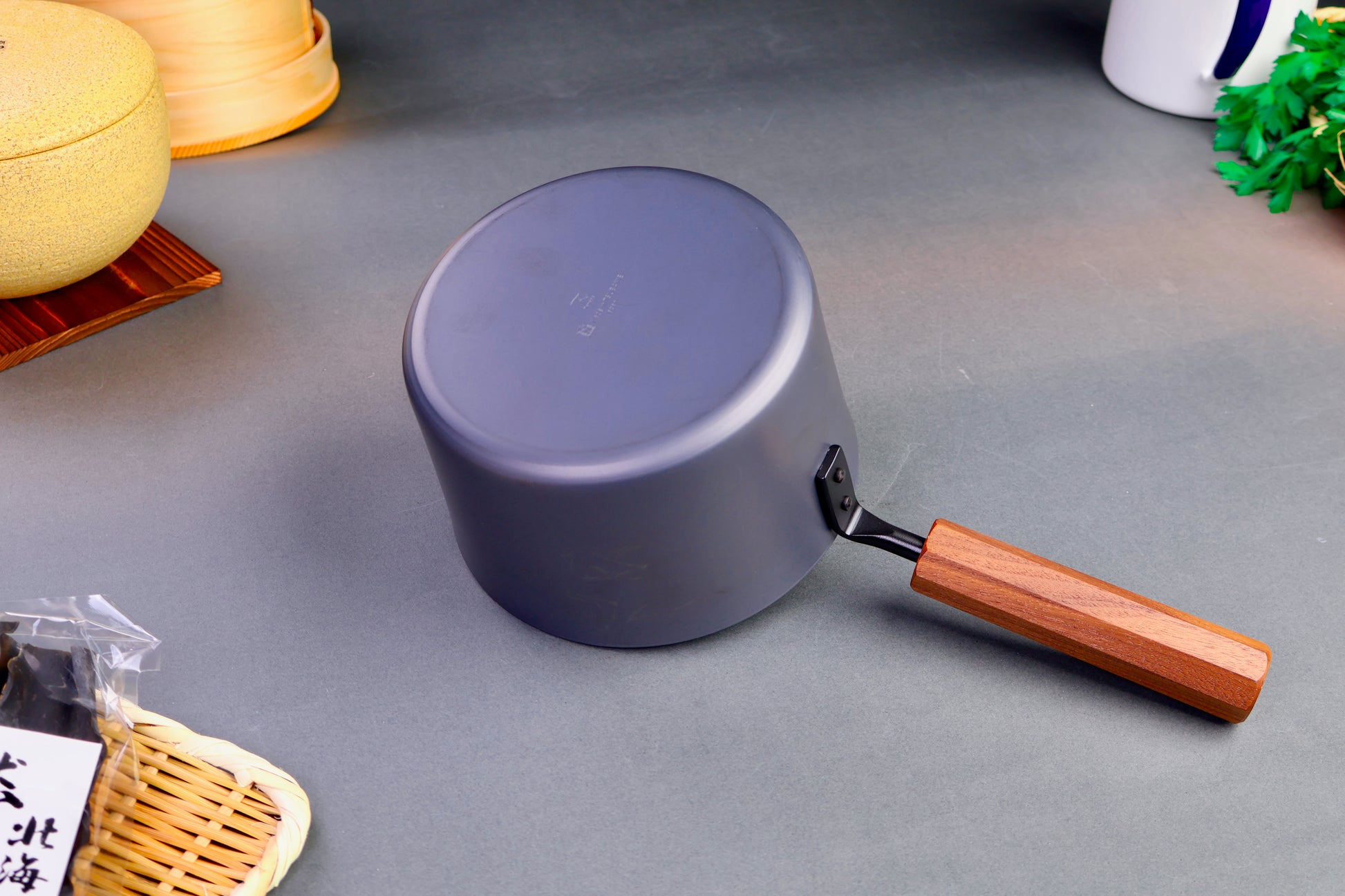 underside of saucepan with wood octagonal handle surrounding kitchenware grey background