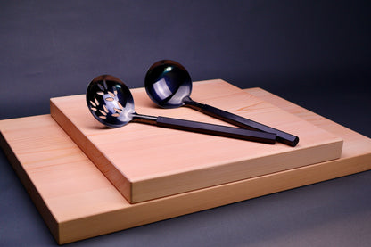 oxidized steel ladles one slotted one solid with wood handles sit atop two hinoki cutting boards with dark grey background 