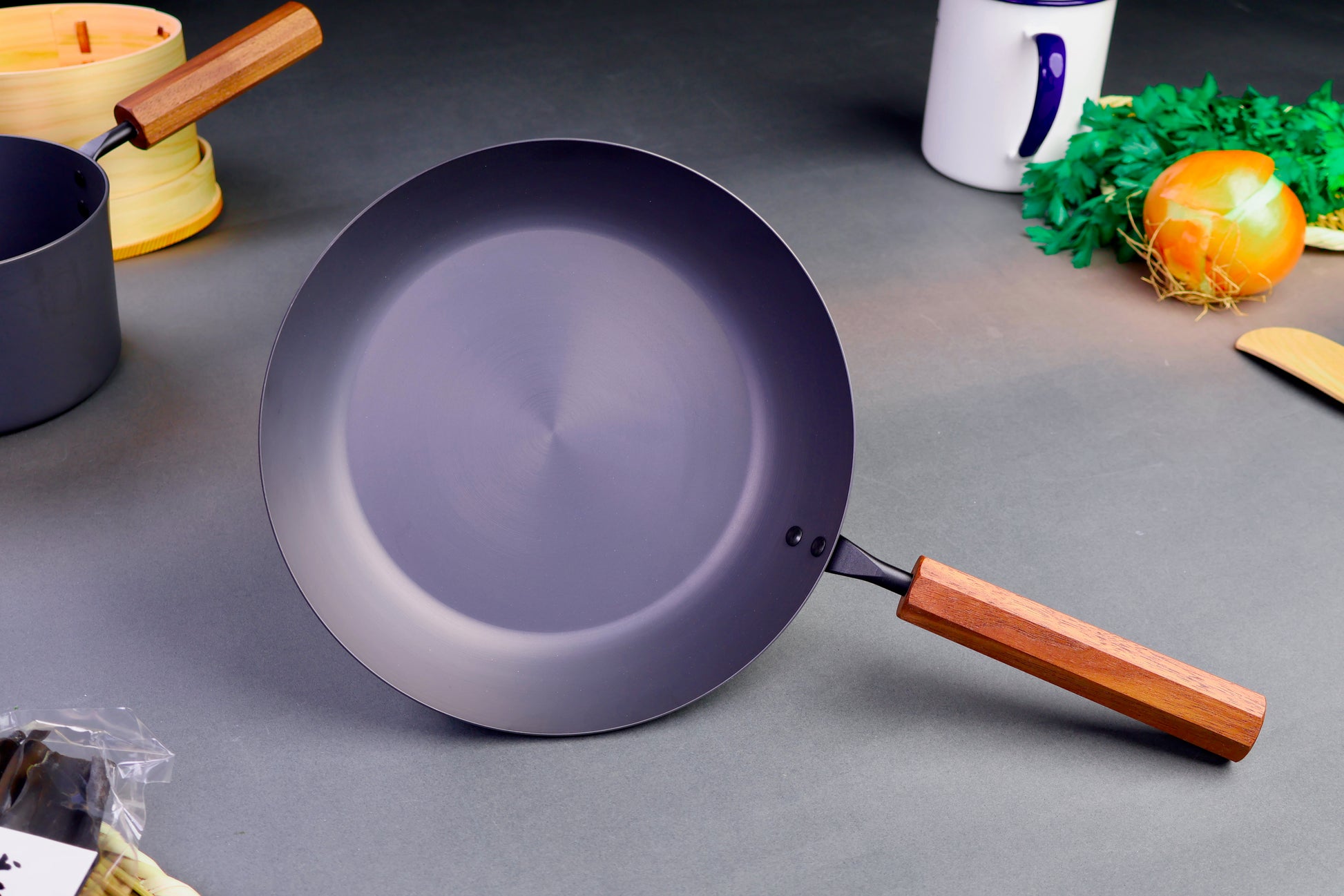 front shot of nitrided iron pan with wood handle octagonal shaped surrounded by Japanese kitchenware with light grey background