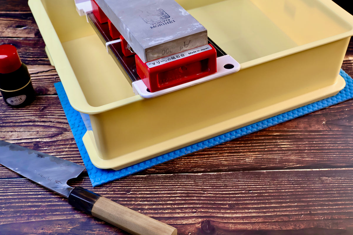 Sharpening station kit — stone holder in tray with whetstone, Japanese knife, and tsubaki oil in use