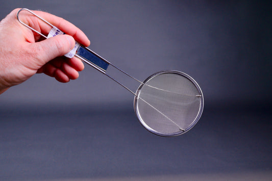 hand holding long handled stainless steel fine mesh skimmer showing thin wire in grey background