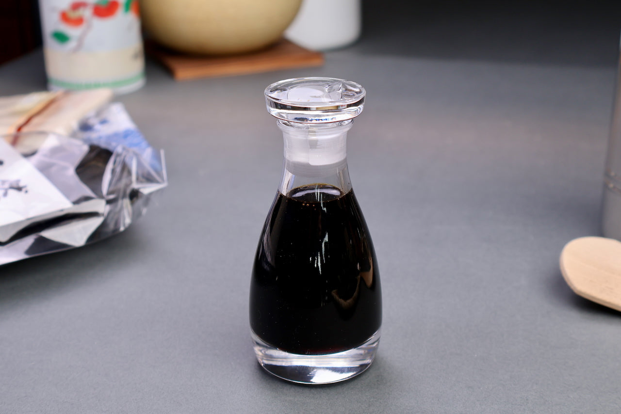 the soy sauce cruet glass container full of soy sauce with circular lid surrounding japanese kitchenware grey background