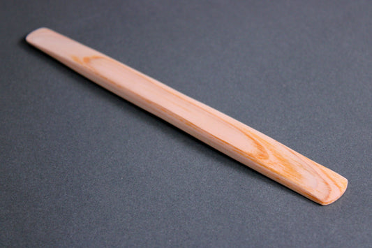 long thin flat natural wood tone hinoki spreader in dark grey backdrop 