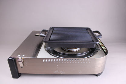 square black nonstick grill sitting on silver portable gas stove with grey background