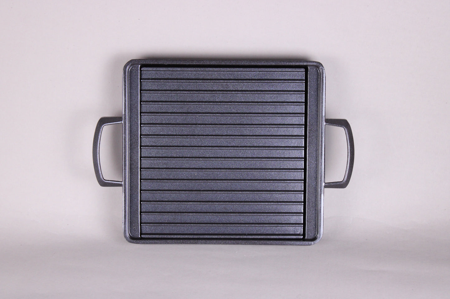 square black grill with 2 handles ridges and removable center plate shown with grey background 