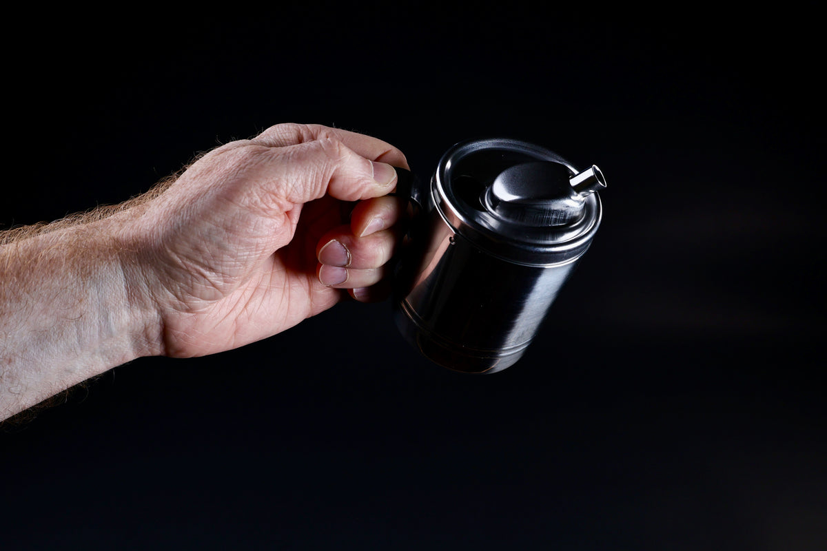 Stainless steel oil cruet small — held in hand at pour angle showing spout and dome lid detail
